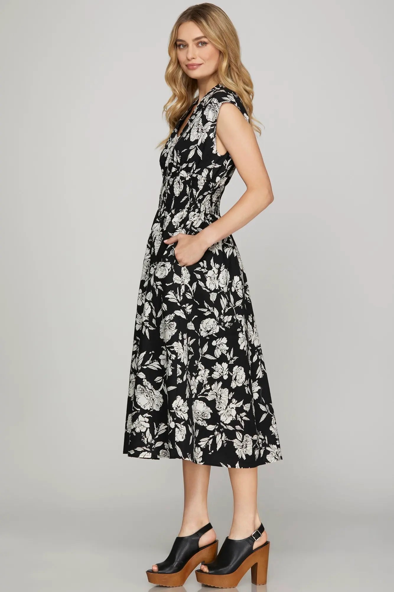 Side view of black and ivory floral smocked waist midi dress with pockets