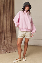 Woman wearing a pink oversized polka dot sweatshirt with a snap-button mock neck and grey bucket hat.