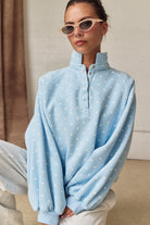 Close-up of woman in light blue polka dot mock neck sweatshirt with snap buttons and sunglasses.