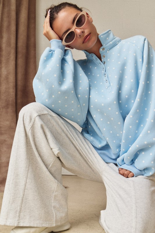 Woman posing in a light blue polka dot sweatshirt featuring balloon sleeves and trendy cat-eye sunglasses.