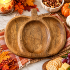 Pumpkin-shaped wooden tray with carved details on a plaid cloth, surrounded by autumn leaves and a lit candle.