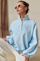 Close-up of woman in light blue polka dot mock neck sweatshirt with snap buttons and sunglasses.