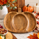 Pumpkin-shaped wooden tray with visible wood grain, styled with fall flowers, decorative pumpkins, and a plaid towel