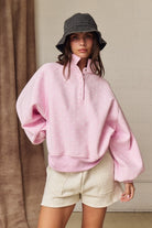 Woman wearing pink polka dot snap-button sweatshirt with balloon sleeves and a black bucket hat.