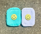Two small zippered pouches with embroidered smiley faces, one in turquoise and one in pale lavender, placed side by side on a gray concrete surface.