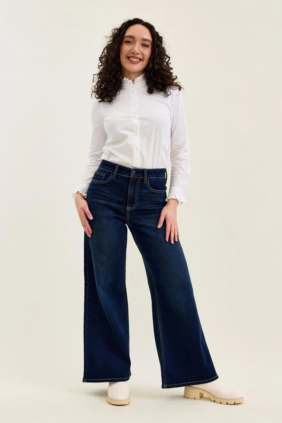Model wearing Judy Blue petite Twilight Blue wide leg jeans with a white blouse and cream boots