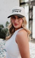 Woman wearing a white cap with text, standing outdoors.