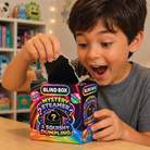 A young boy with dark hair wearing a gray t-shirt is excitedly opening a colorful 'Mystery Steamer & Squishy Dumpling' blind box. The box features a vibrant rainbow design with a black inner flap being pulled open.