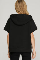 Back view of a women’s black quilted short-sleeve hoodie top with a relaxed fit and hood. Stylish athleisure piece designed for comfort and everyday casual wear.