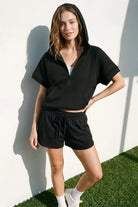 Women’s black quilted half-zip hoodie top paired with black drawstring shorts and white sneakers. Lightweight matching set ideal for summer, travel, lounging, and casual everyday style.