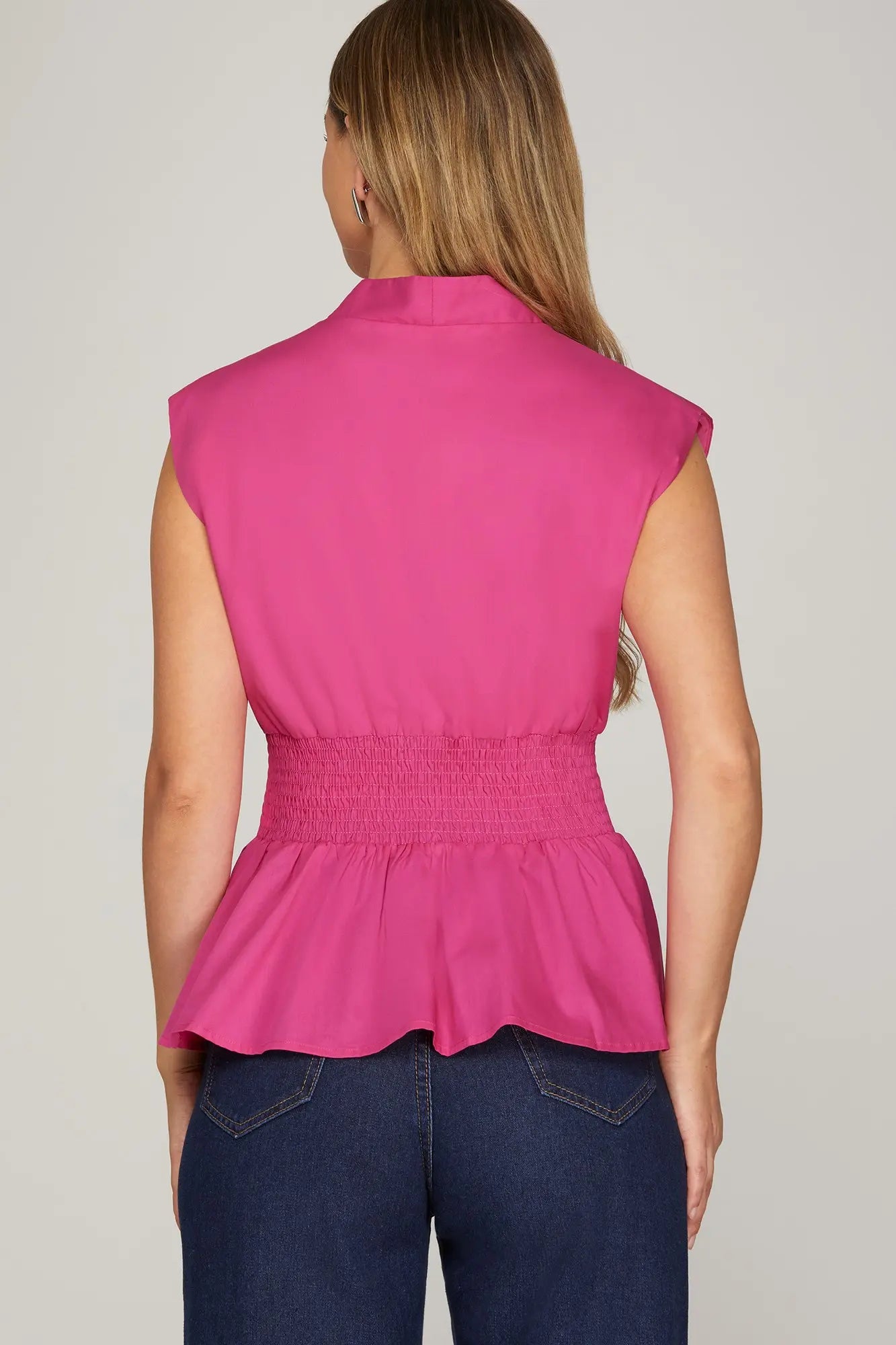 Back view of a fuchsia drop shoulder smocked waist peplum top showing wide elastic smocking detail and flared hem, paired with dark wide-leg denim
